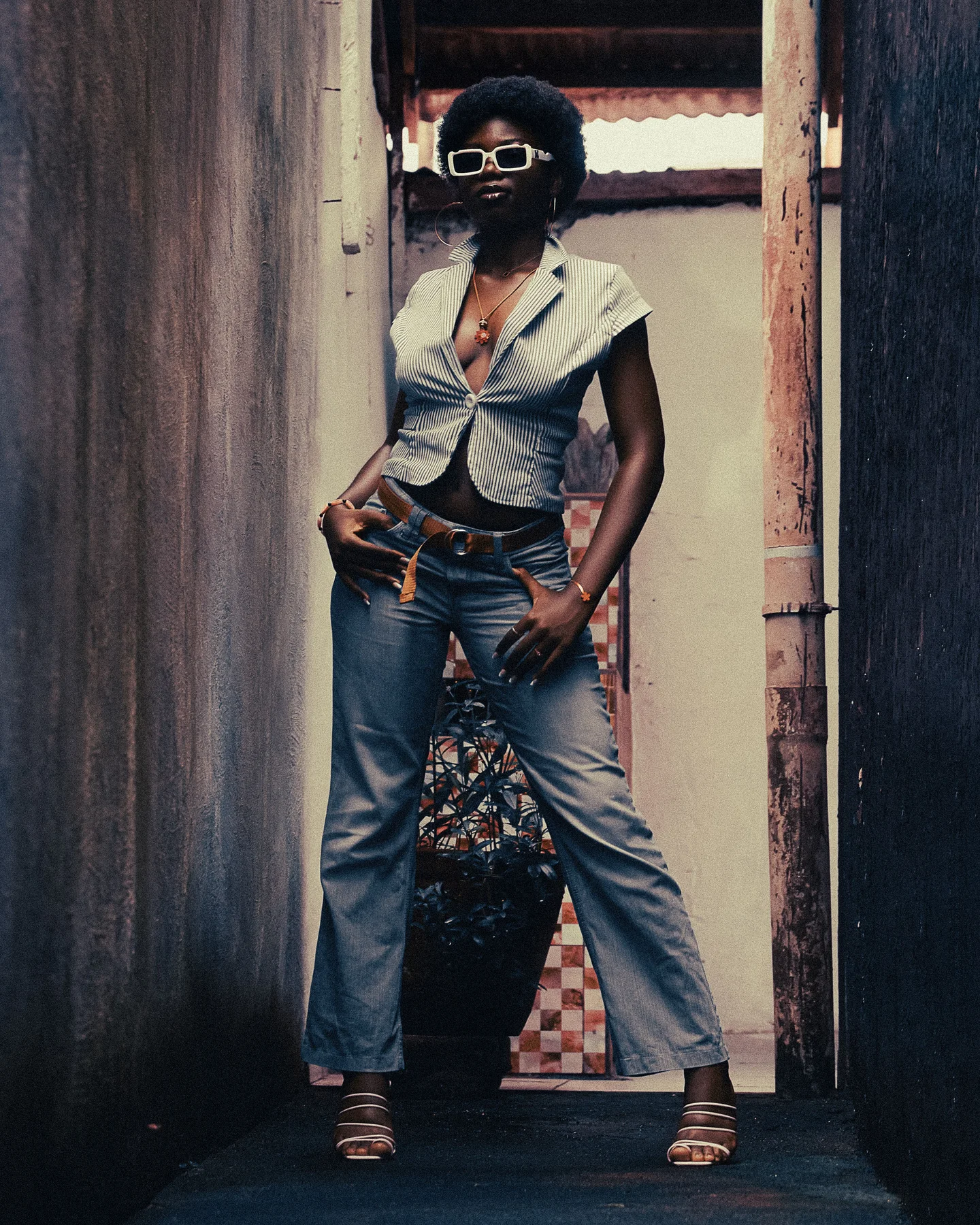 Femme en veste rayée et jean posant dans un passage architectural