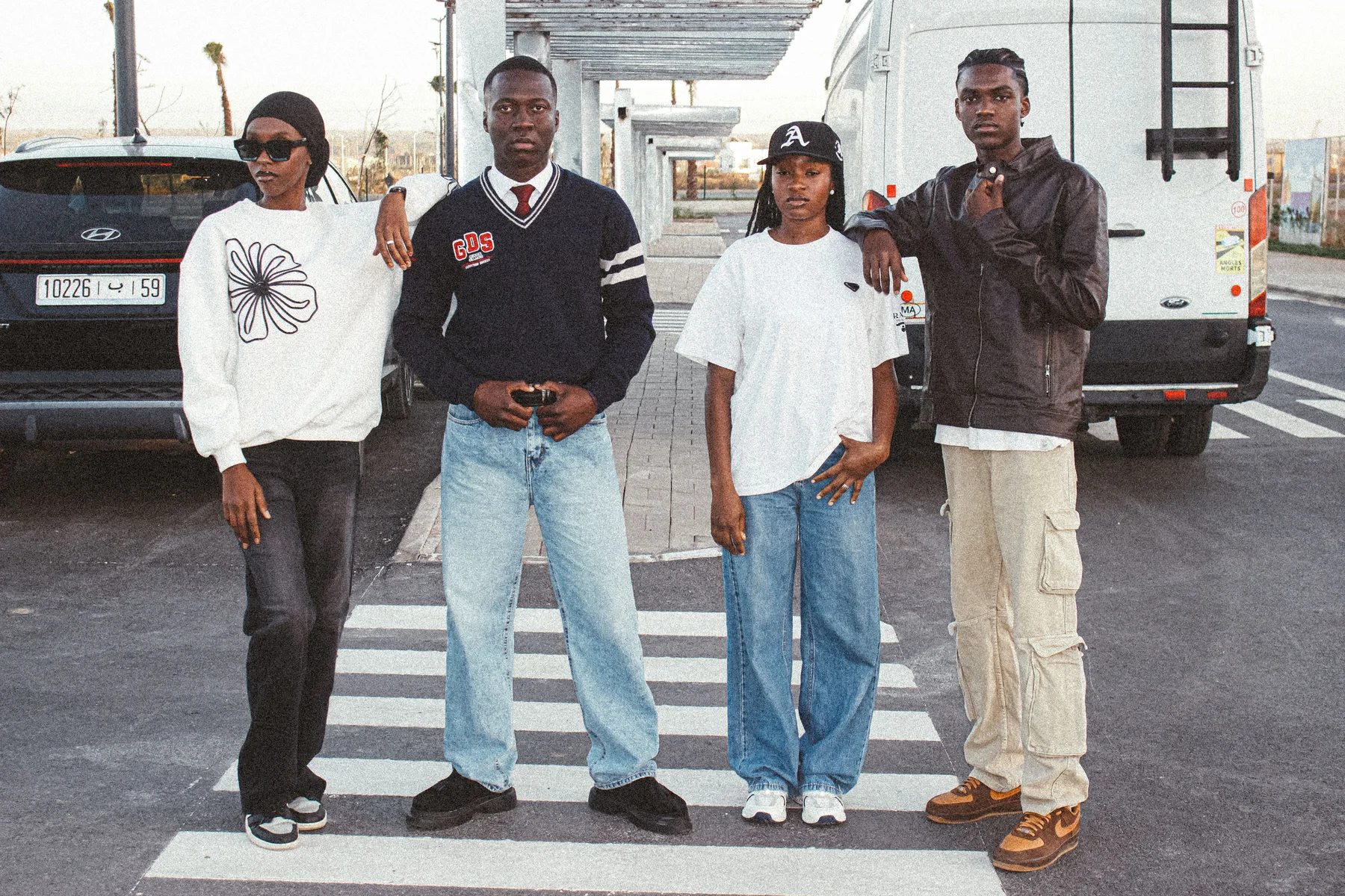 Quatre jeunes adultes posant dans la rue devant des véhicules